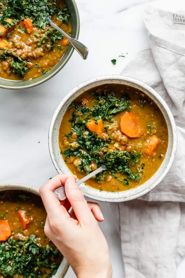 a hand scooping a spoon in a bowl of slow cooker lentil soup 