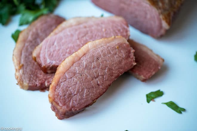 Slow Cooker Corned Beef Recipe, tender, juicy meat with spices on top on cutting board.