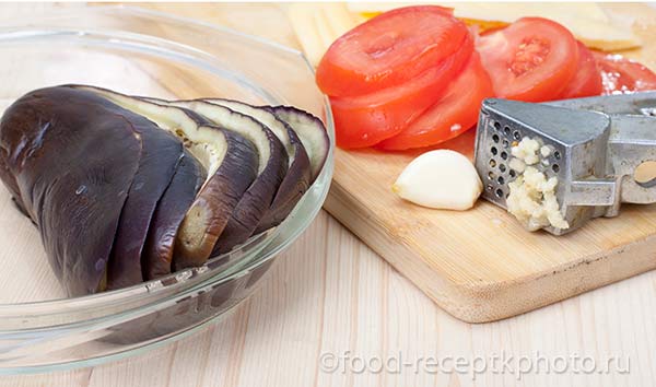 Ингредиенты для запеченных баклажан: помидор,чеснок,сыр,баклажан на разделочной доске