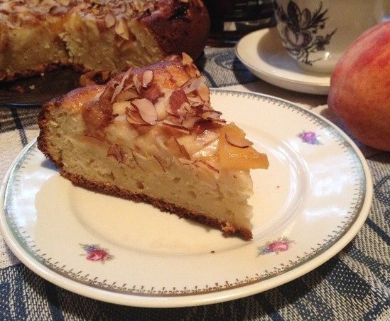 Кусочек пирога с персиками и миндальными хлопьями на тарелке