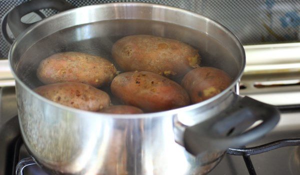 Неочищенные клубни картофеля в кастрюле с водой на плите