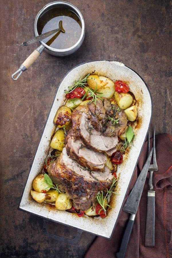 Barbecue marinated lamb roast with tomatoes, potatoes and herbs in a roasting dish stock photo
