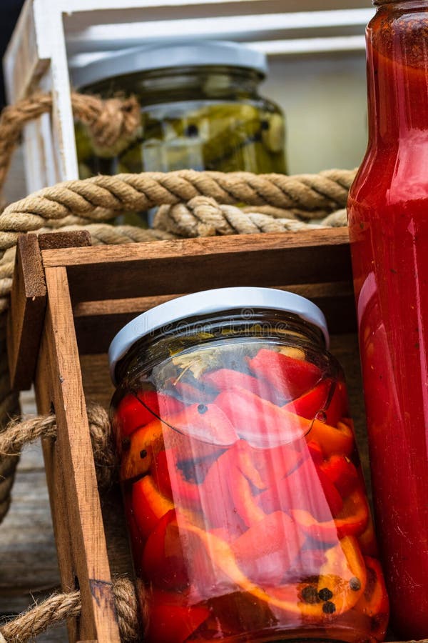 Glass jars with pickled red bell peppers and bottles with tomatoes sauce isolated in a rustic composition. Jars with variety of royalty free stock image