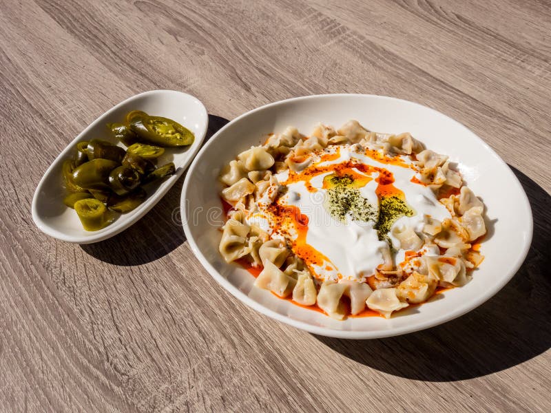 Turkish Manti with green hot pickled peppers, tomato sauce, yogurt and mint. Plate of traditional Turkish food. Top view stock photography