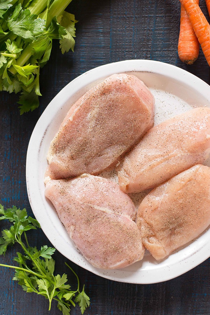 Ingredients ready for the slow cooker chicken noodle soup, including seasoned chicken breasts, celery, italian parsley, and carrots.