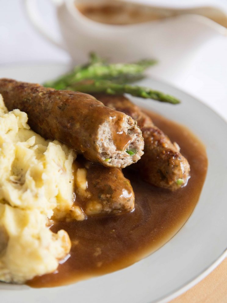 closeup shot of sausage sliced open with gravy dripping down with mash and asparagus