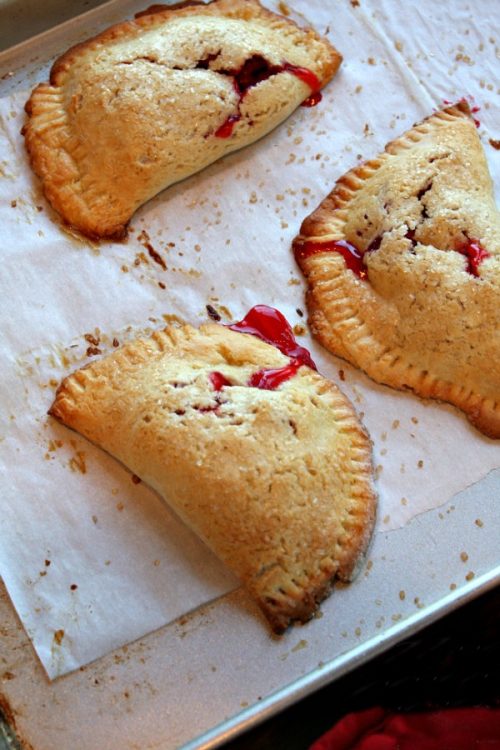Three baked Berry Hand Pies on a baking sheet lined with parchment paper
