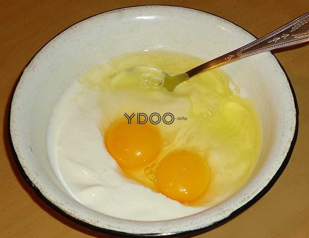 два вбитых в миску куриных яйца со сметаной, внутри миски столовая ложка