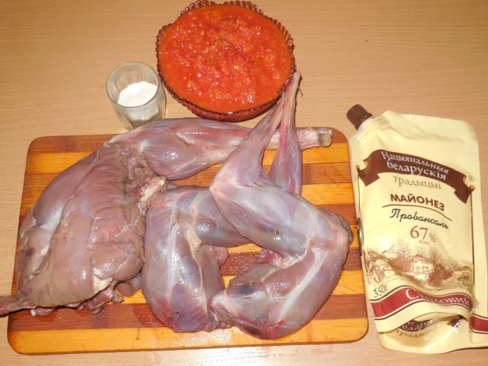 сырая тушка зайца на полосатой деервянной разделочной доске, пачка майонеза, аджика в пиале и солонка на столе