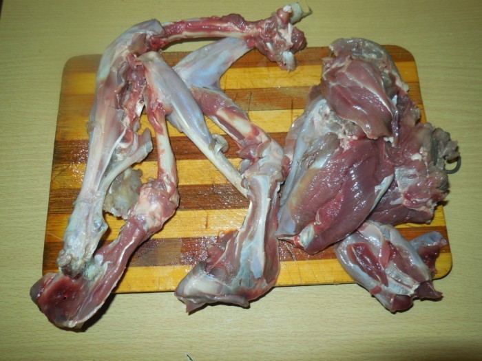 сырое мясо зайца, отделенное от костей, на полосатой деревянной разделочной доске на столе